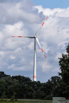 A vertical portrait of a big windmill standing tall above the trees with a cl Stock Photos
