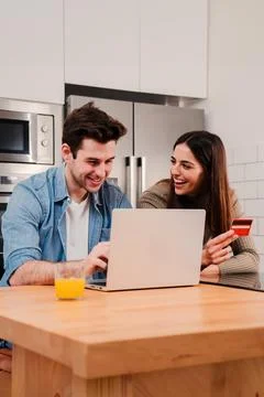 Vertical portrait of a couple smiling using a laptop and a credit card to buy on Stock Photos