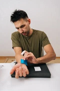 Vertical portrait of man applying blue elastic therapeutic tape to wrist for Stockfoto's