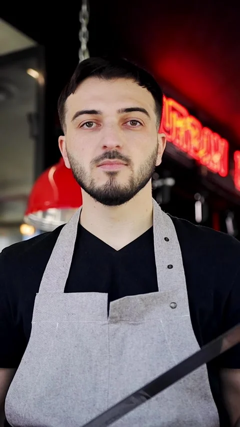 Vertical portrait of a man with a large meat slicing knife poses for the camera Stock Footage 280386466