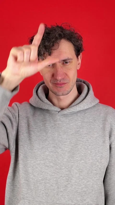 Vertical portrait man raises hand making loser gesture, L sign on forehead 動画素材 304761331