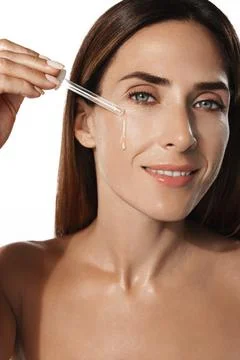 Vertical portrait of middle aged, 40s woman, applies skin care serum, argan oil Stock Photos