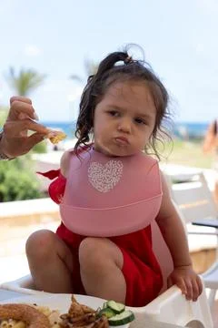Vertical portrait of mother feeding grumpy little girl at restaurant Foto stock