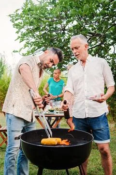 Vertical portrait of a pair of middle aged men cooking meat on a barbeque good Stock Photos