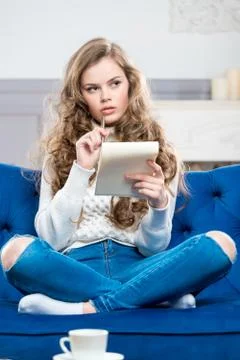Vertical portrait of a pensive girl with a notebook sitting on the couch Stock Photos