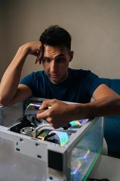 Vertical portrait of puzzled technician upgrading desktop computer by installing Stock Photos