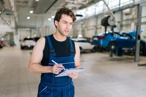 Vertical portrait of serious auto mechanic male checking car with tablet in Stock Photos