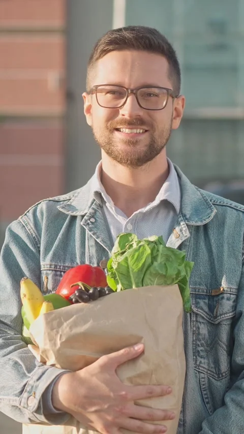 Vertical portrait. Smiling Caucasian man in glasses holding paper grocery bag Stock Footage 310728892