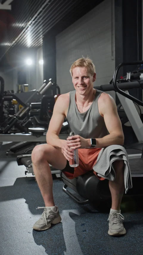 Vertical Portrait of Smiling Man Sitting in Gym Holding Water Bottle Stock Footage 339886733