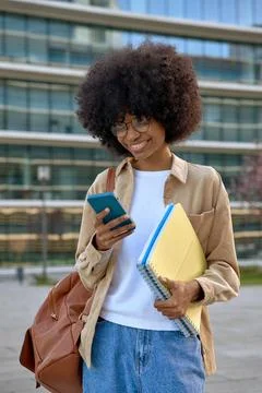 A vertical portrait of student using looking at her phone on city background Stock Photos