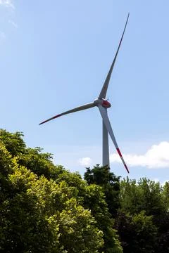 A vertical portrait of a windmill standing high above the trees in a blue sky Stock Photos