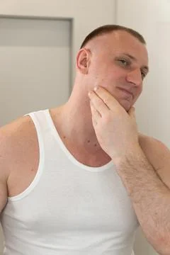 Vertical portrait of young man looking in mirror after shaving Stock Photos