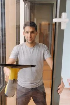 Vertical portrait of young man using a cordless vacuum cleaner to clean Stock Photos