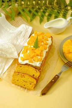 Vertical pound cake with mango and whipped cream on yellow background, home c Stock Photos
