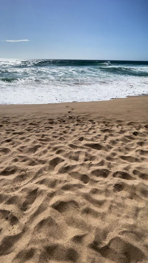 VERTICAL, POV, LENS FLARE: Man walking across sandy beach toward rolling waves Stock Footage 334011602