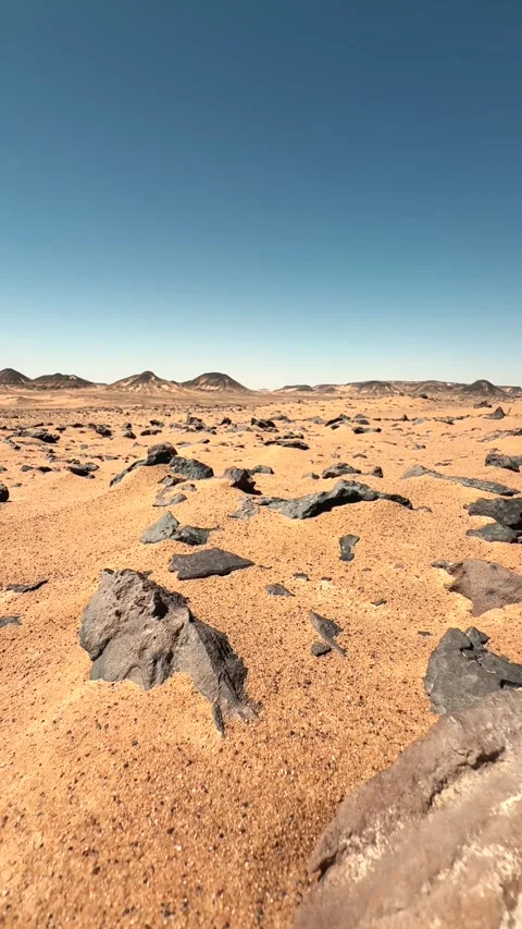 Vertical pull-back close up motion above black basalt stones in the sand of Stock Footage 340867480