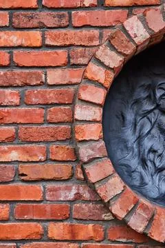 Vertical of red brick wall with half circle opening to black motif of wavy lions Stock-Fotos