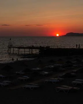 Vertical red sunset over Mediterranean Sea with pier and beach resort silho.. 스톡 사진