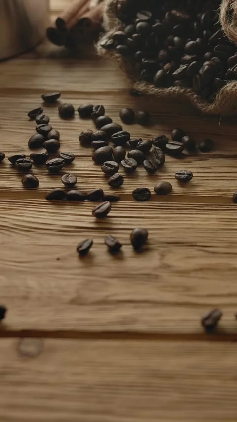 Vertical of Roasted coffee beans falling down with jute sack on wooden table Stock Footage 276920576