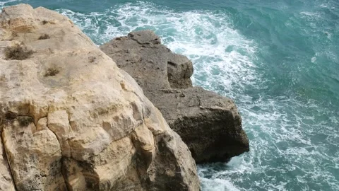 Vertical rock cliff face towers over surf below stone texture detail waves Stock Footage 341800088