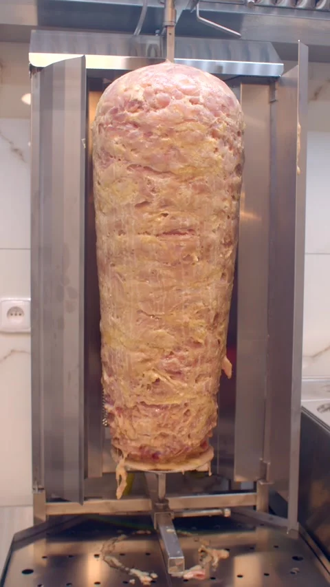 Vertical rotating doner kebab meat on stainless rotisserie in commercial kitchen Stock Footage 336535521