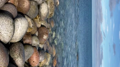 Vertical: Rounded stones lying on north sea shore, calm water Stock Footage 231509162
