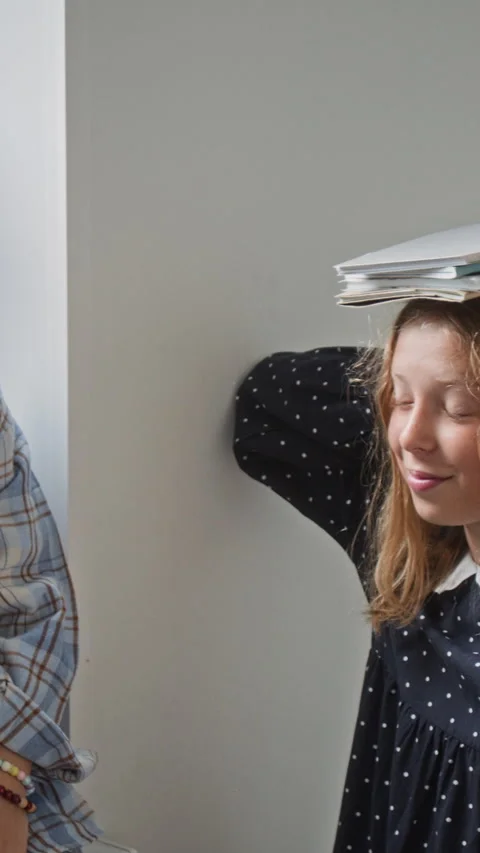 Vertical of Schoolgirl Balancing Notebooks on Head While Talking with Friend 動画素材 345226923