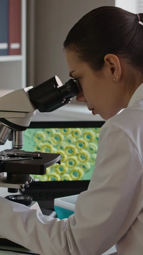 Vertical of Scientist Analyzing Cells in Microscope and Using Laptop in Lab Stock Footage 332358345