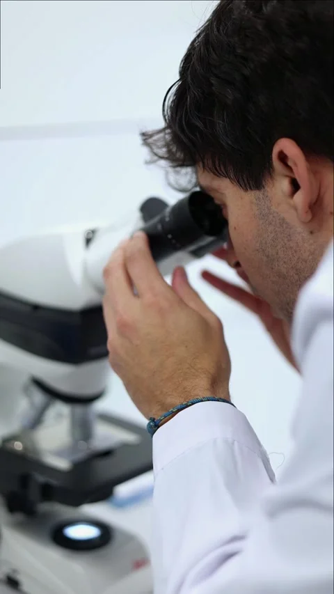 Vertical Scientist analyzing samples under microscope in laboratory Stock Footage 296886225