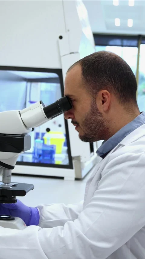 Vertical Scientist analyzing samples under microscope in modern laboratory Stock Footage 296886271