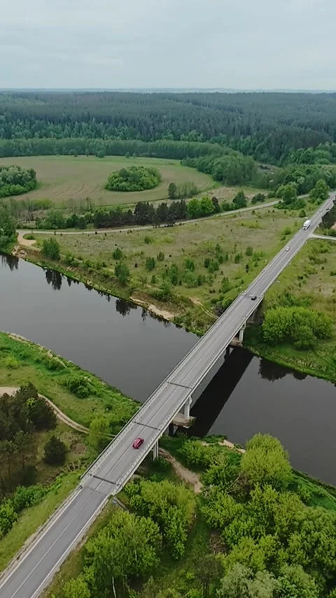 Vertical screen aerial bridge crossing river, red car, rural commuter scene Stock Footage 325753604