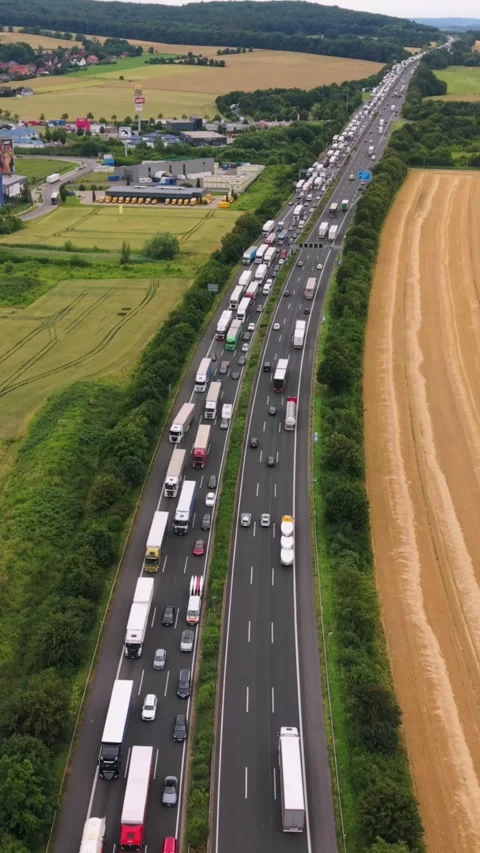 Vertical screen. Aerial perspective of trucks lined up on a highway, with lush Stock Footage 346552152