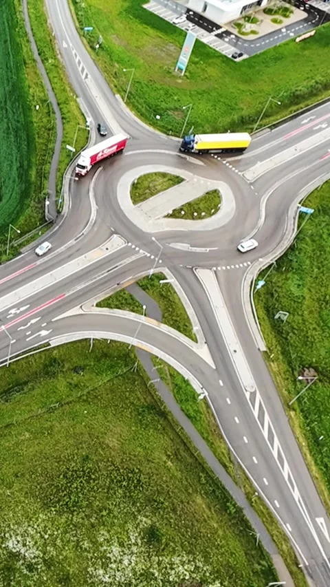 Vertical screen aerial view roundabout freight convoy threading through green Stock Footage 323778307