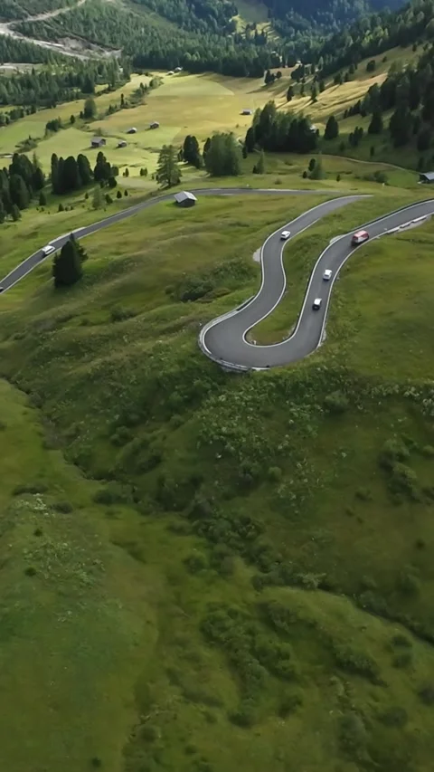 Vertical screen Aerial view winding mountain road with sunlit green meadows and Видео 323890798