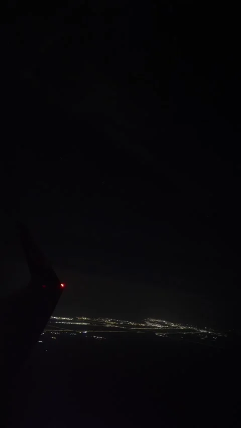 Vertical screen airplane wing glows in darkness with city lights below mild turb Stock Footage 310467128