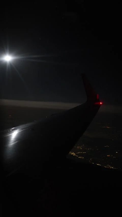 Vertical screen airplane wing reflects moonlight in deep night sky as red tip gl Stock Footage 310467670