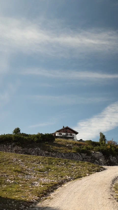 Vertical screen alpine cottage stands on hilltop above winding gravel road surro Stock Footage 318219915