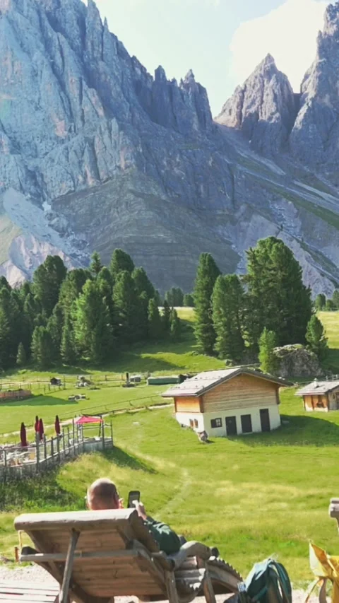 Vertical screen of alpine meadow and village buildings beneath jagged Dolomites Stock Footage 319669725