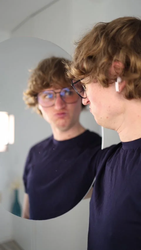 Vertical screen angry young man grimaces and scowls at his reflection in the mir Stock Footage 313268761