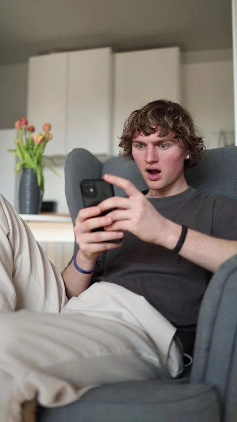 Vertical screen: Astonished young man holding smartphone, shocked by unexpected  Stock Footage 302632203