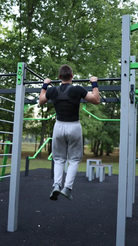 Vertical screen athlete performs pull ups on outdoor bar strengthening back and  Stock Footage 316700232