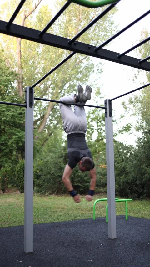 Vertical screen athletic guy lifts legs while hanging on bar in outdoor park gym Stock Footage 316700861