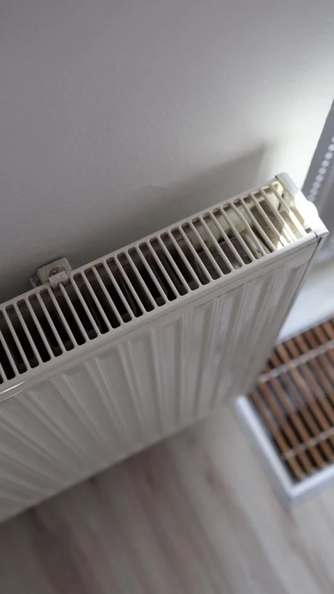 Vertical screen beginning of heating season white radiator near wall lit by sunl Video stock 312175640