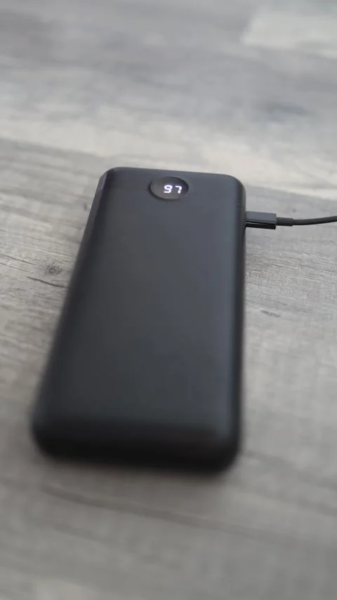 Vertical screen: A black power bank is charging, connected to a cable on a woode Stock Footage 303907508