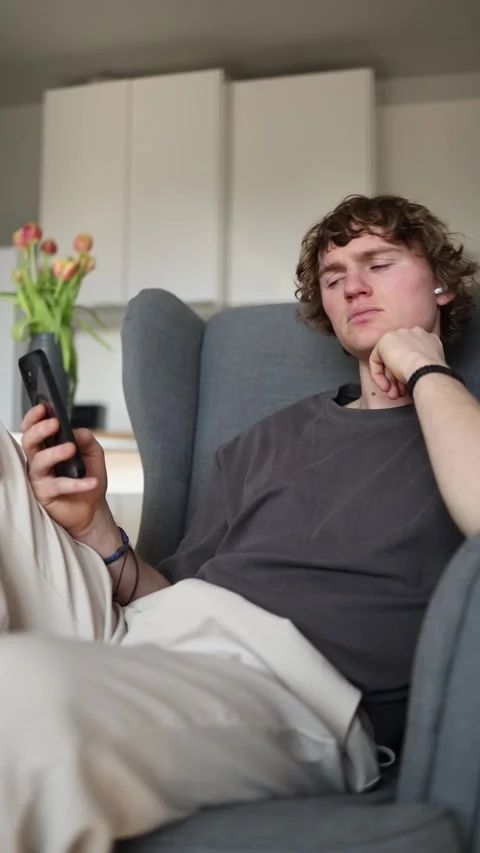Vertical screen: Bored young man holding smartphone, feeling uninterested and ti Stock Footage 302632331