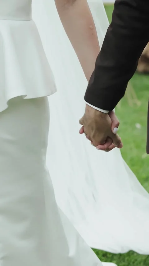 Vertical screen: A bride and groom stroll hand in hand in a lush green field Stock Footage 308395438