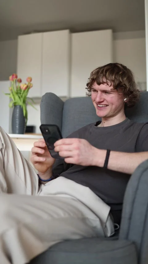 Vertical screen: Cheerful young man smiling happily at his smartphone, enjoying  Stock Footage 302632371