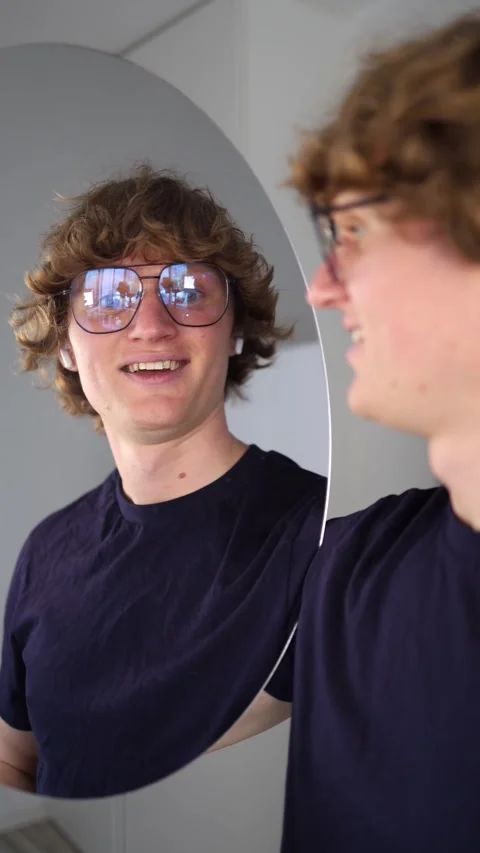 Vertical screen cheerful young man smiles at his reflection holding both hands u Stock Footage 313268896