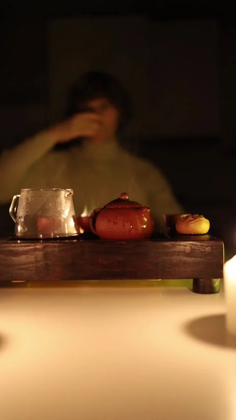 Vertical screen: A clay teapot and glass pitcher on a wooden tray in warm candle Stock Footage 299379046