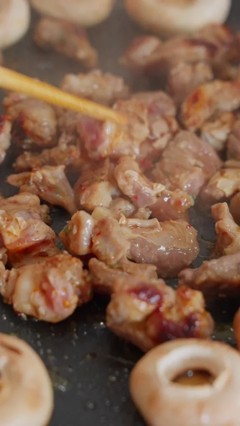 Vertical screen close-up of chopsticks flipping pieces of marinated mutton on an Stock Footage 341650785